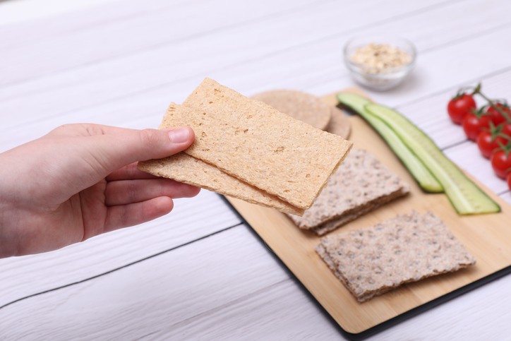 Woman holding tasty crispbread at white wooden table, closeup