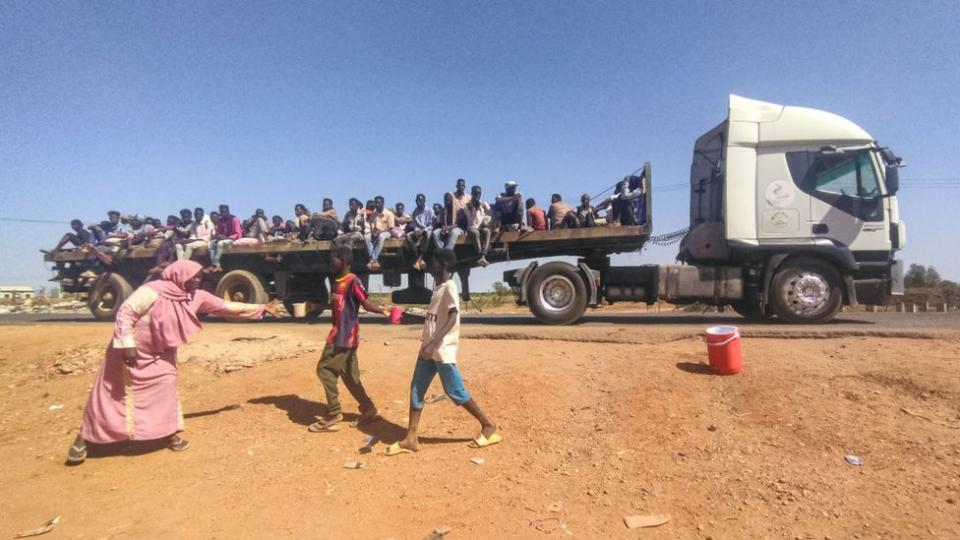 People displaced by the conflict in Sudan ride on the back of a truck moving along a road in Wad Madani, the capital of al-Jazirah state