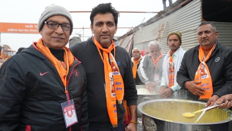 Two men in orange scarves stand next to a food service line.
