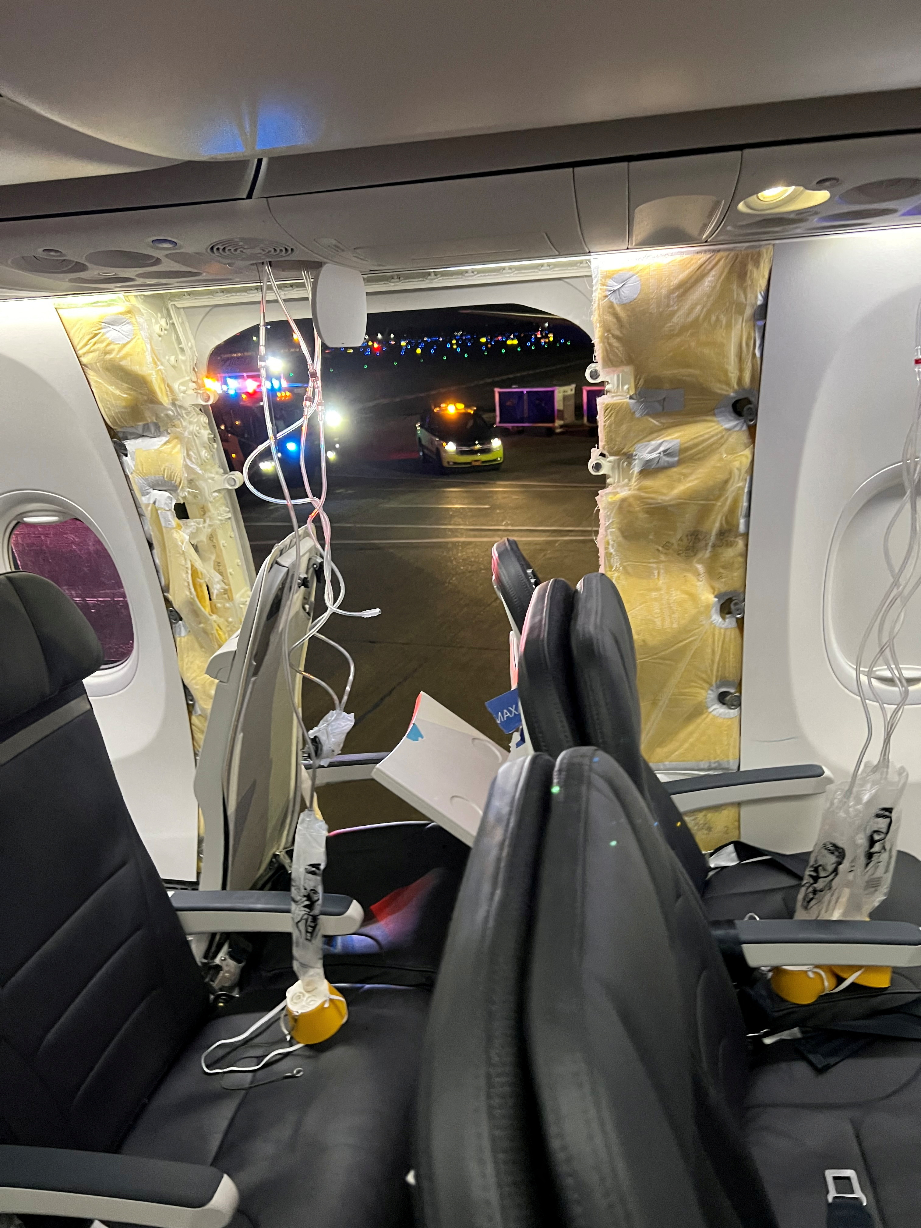 Passenger oxygen masks hang from the roof next to the missing door on the Alaska Airlines flight