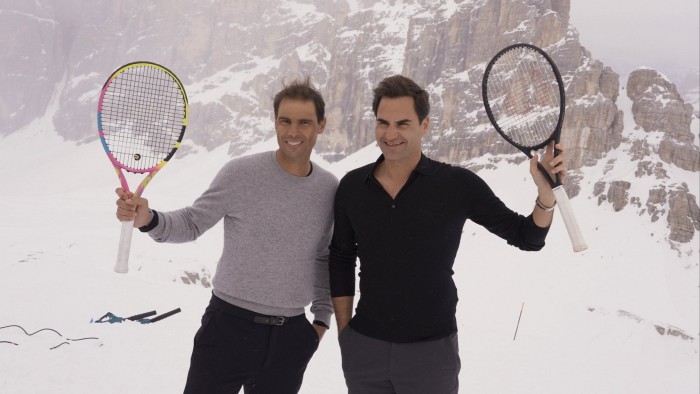 Two men holding tennis racquets against a snowy mountain backdrop